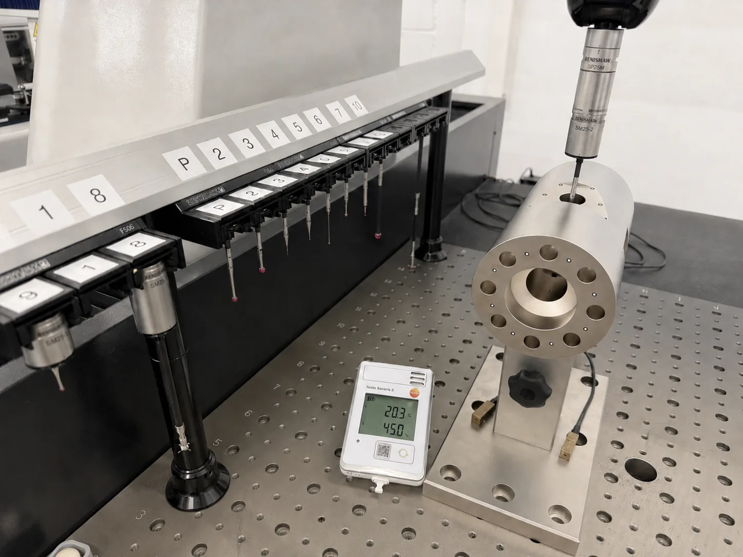 Measuring room at CSL: Renishaw probe above a part on the surface plate, probe changer and temperature logger showing 20.3 °C