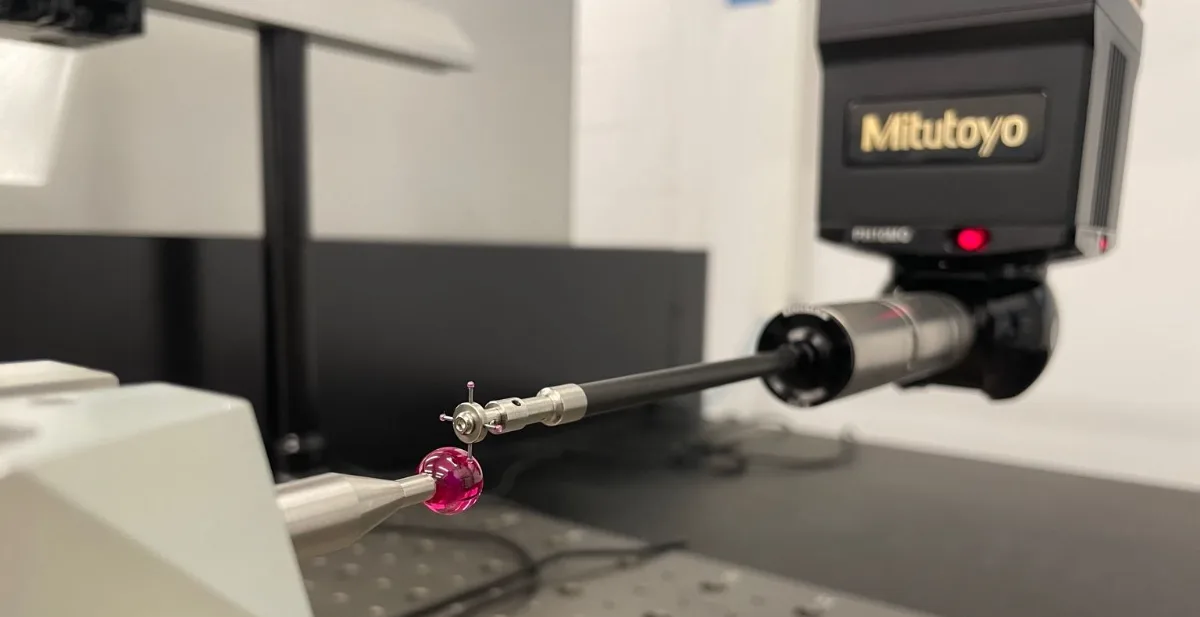Long star stylus on the articulating probe head of a coordinate measuring machine — the stylus tip touches the calibrated reference sphere